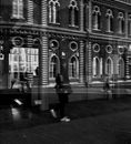Black and white through glass of blurred people walking on city street against exterior of old fashioned mansion in daytime