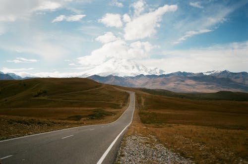 Wavy road in high mounts under blue cloudy sky