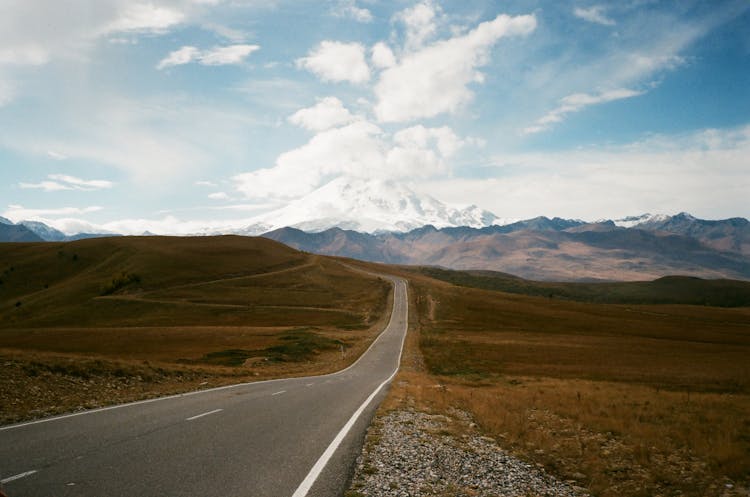 Wavy Road In High Mounts Under Blue Cloudy Sky