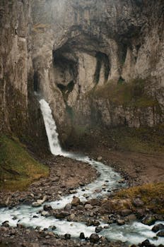 A magnificent waterfall cascades down rugged rocks into a flowing creek in a scenic outdoor landscape.