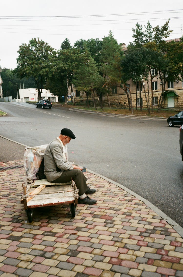 Unrecognizable Senior Man Resting On Old Garden Cart Near Road