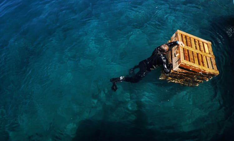 Anonymous Man In Wet Suit Swimming In Ocean With Box