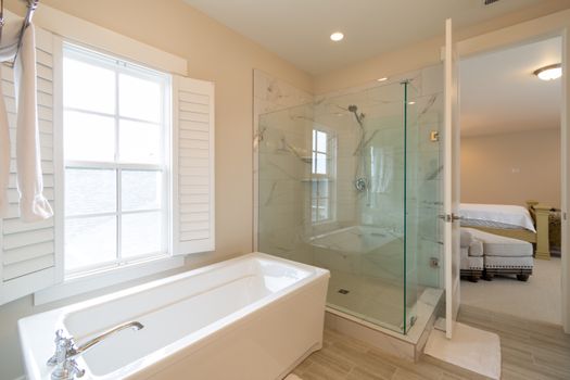 Bright modern bathroom with a bathtub and glass shower next to bedroom.