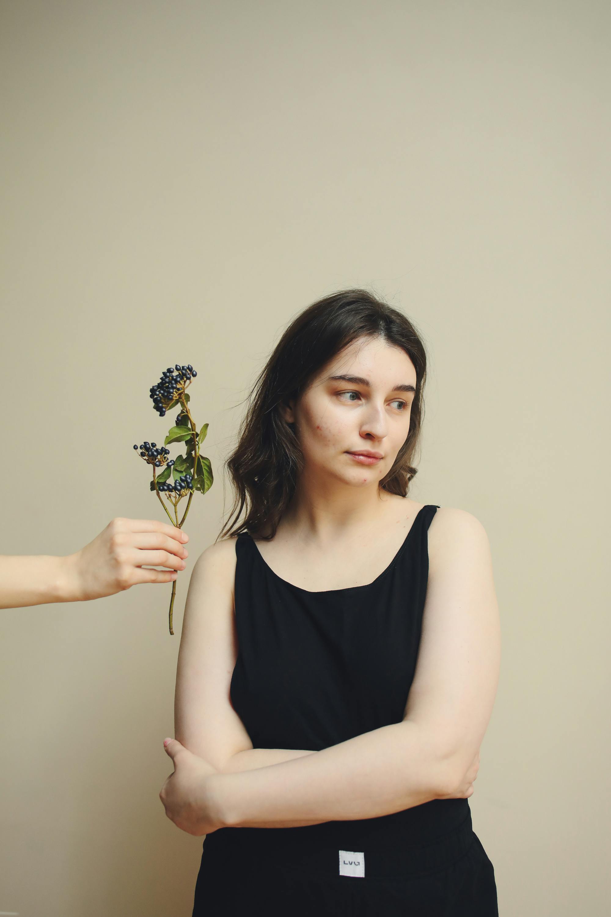 Contemplative woman in black dress with a flower, arms crossed, indoors.