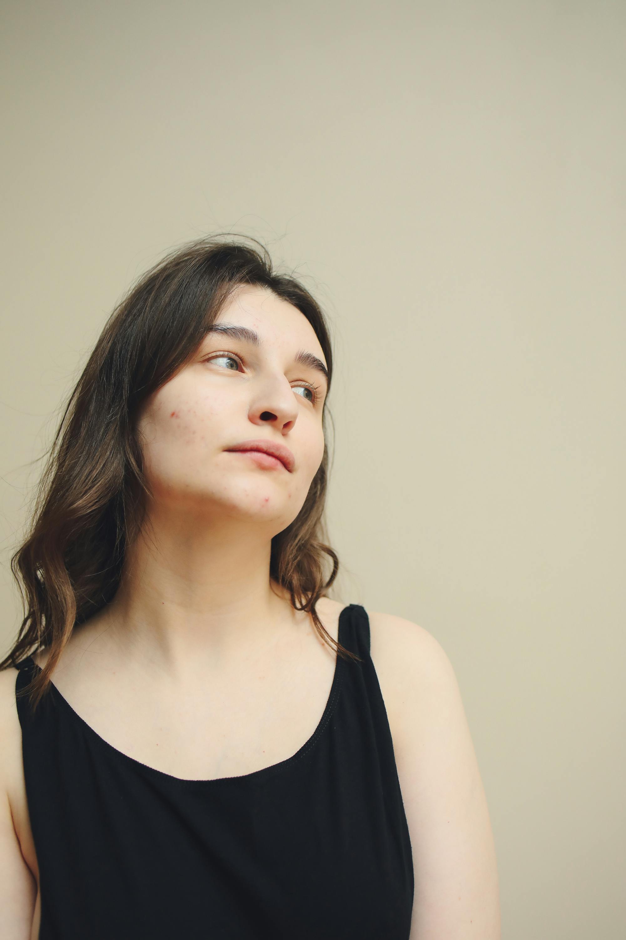 一位年轻女子身着黑色背心，背景朴素，神情若有所思