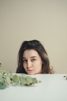 Subtle portrait of a young woman with eucalyptus leaves in soft lighting.