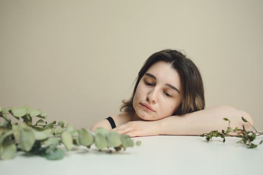 一位沉思中的女子将头靠在被树叶环绕的桌上，流露出孤独与沉思