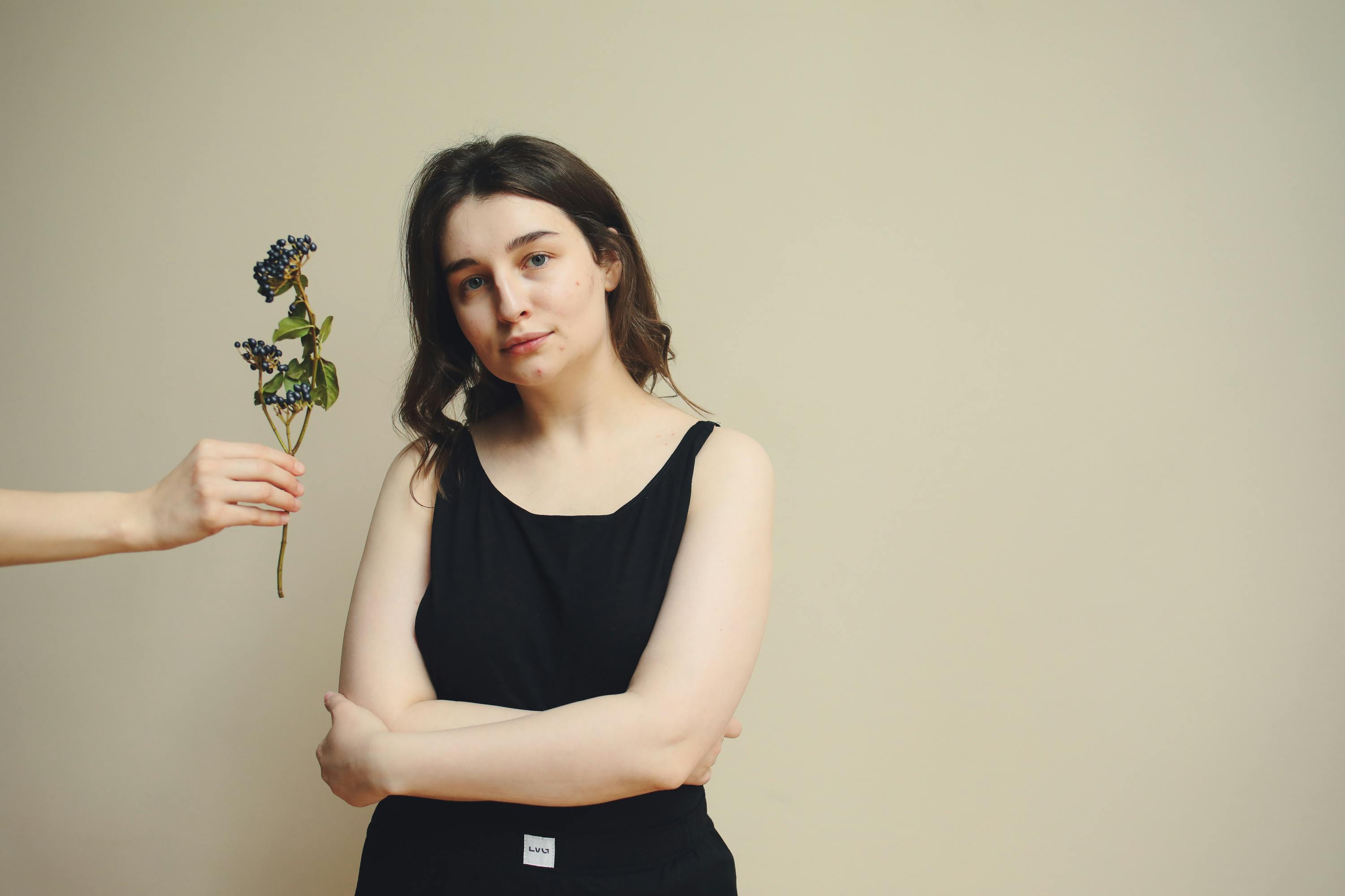 A woman indoors poses with crossed arms and holds a berry branch.