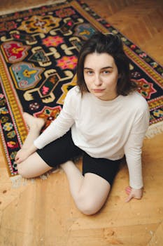 Young woman posing indoors on a colorful rug, exuding confidence.