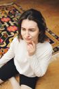 一个女人穿着白衬衫，若有所思地坐在彩色地毯上