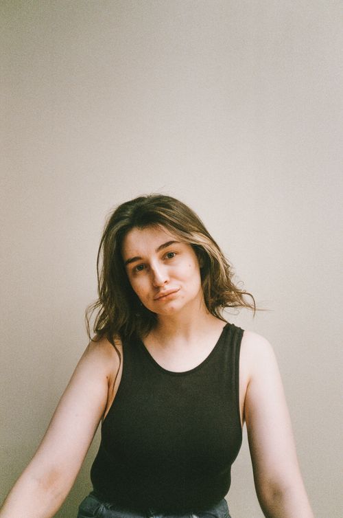 Free A young woman with long hair in a tank top posing thoughtfully indoors. Stock Photo