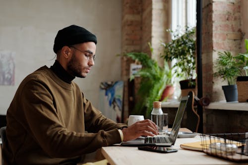 Free Man in Brown Sweater Using a Laptop  Stock Photo