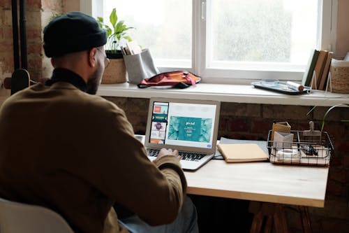 Backview of Man in Brown Sweater Using a Laptop