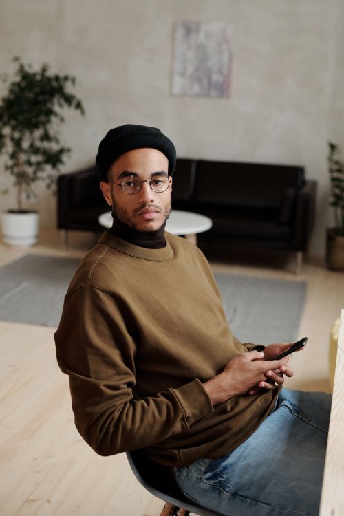 Free Young man in cozy space holding phone, wearing casual stylish outfit. Stock Photo