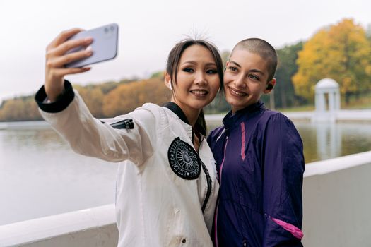 两名女子微笑着在宁静的秋湖旁自拍，享受着这一天