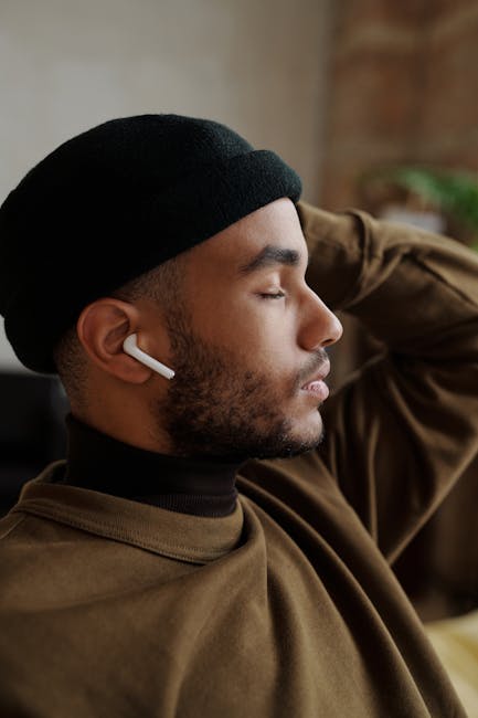 Side profile of a fashionable man enjoying music with earbuds in a cozy indoor setting.