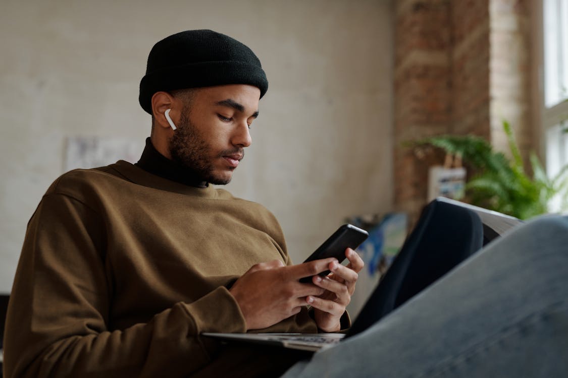 Man in Brown Long Sleeve Shirt and Black Knit Cap Holding Black Smartphone