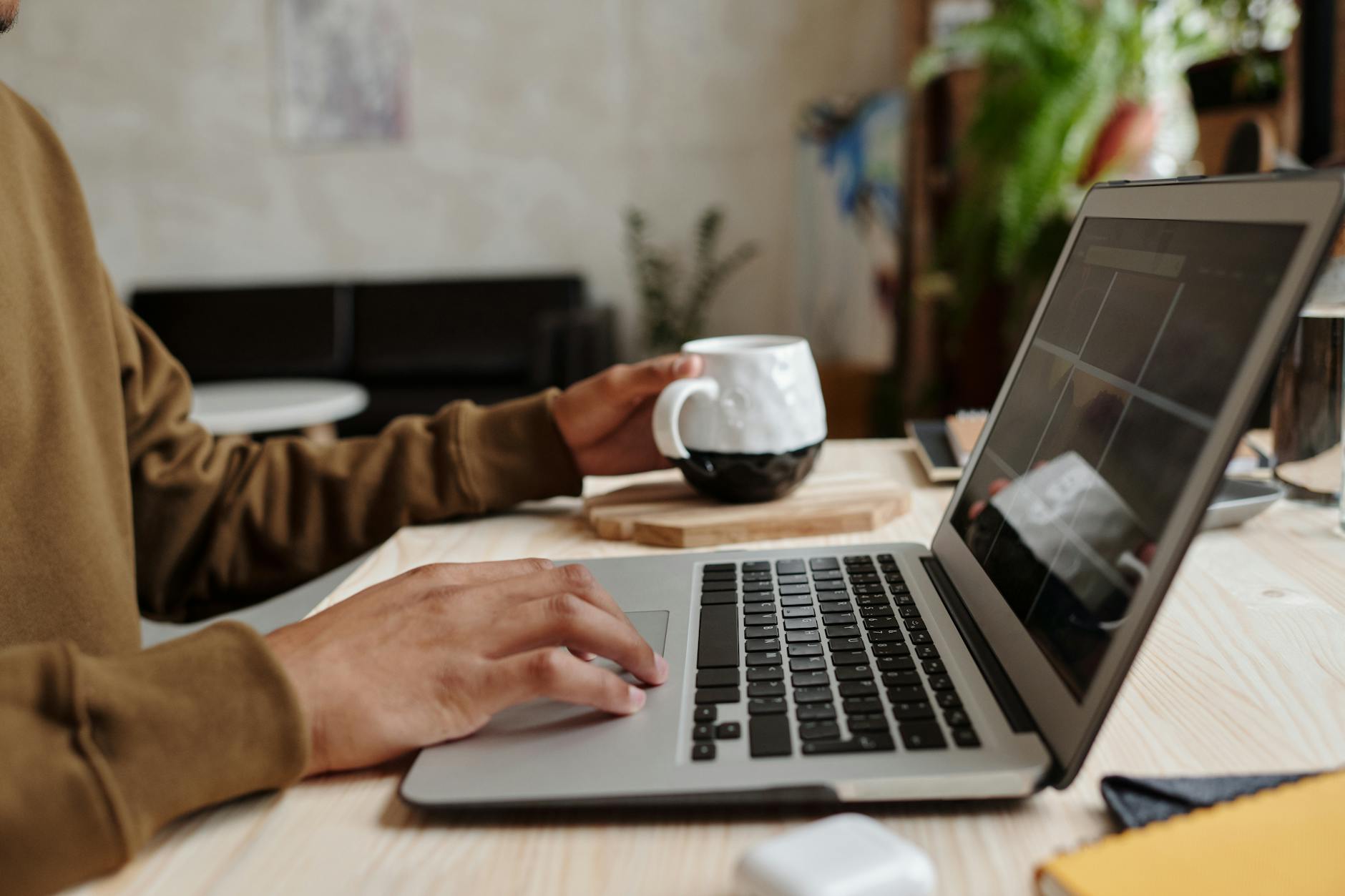 Close-up of a person using a laptop with a coffee mug on a wooden table, ideal for remote work concept.