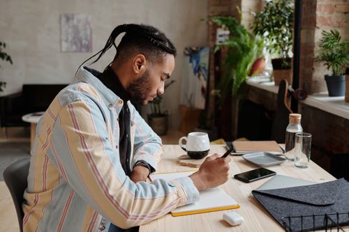 Free Focused young man studying at home office desk with plants and coffee. Stock Photo