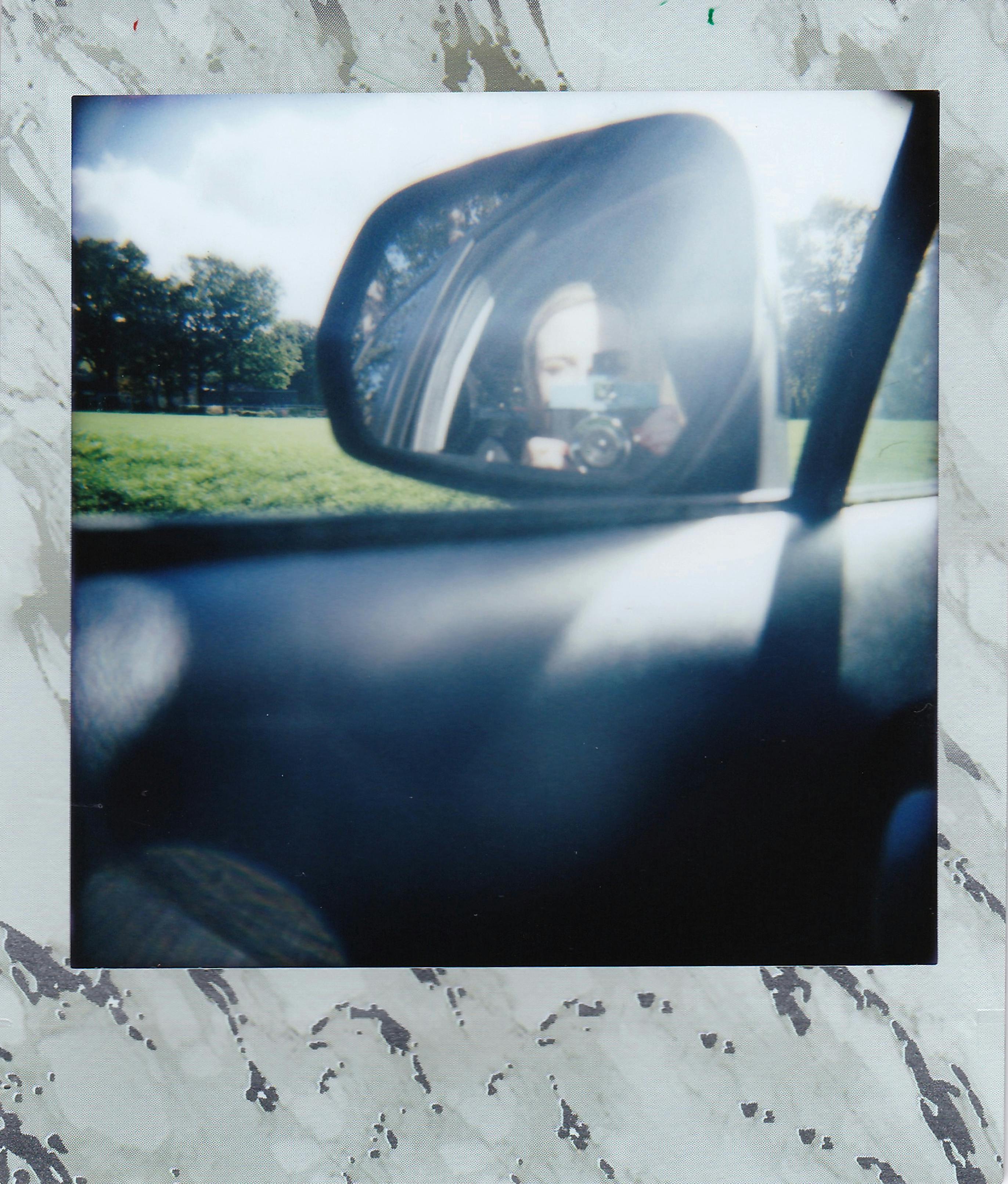 A creative self-portrait taken through a car's side mirror with a scenic outdoor background.