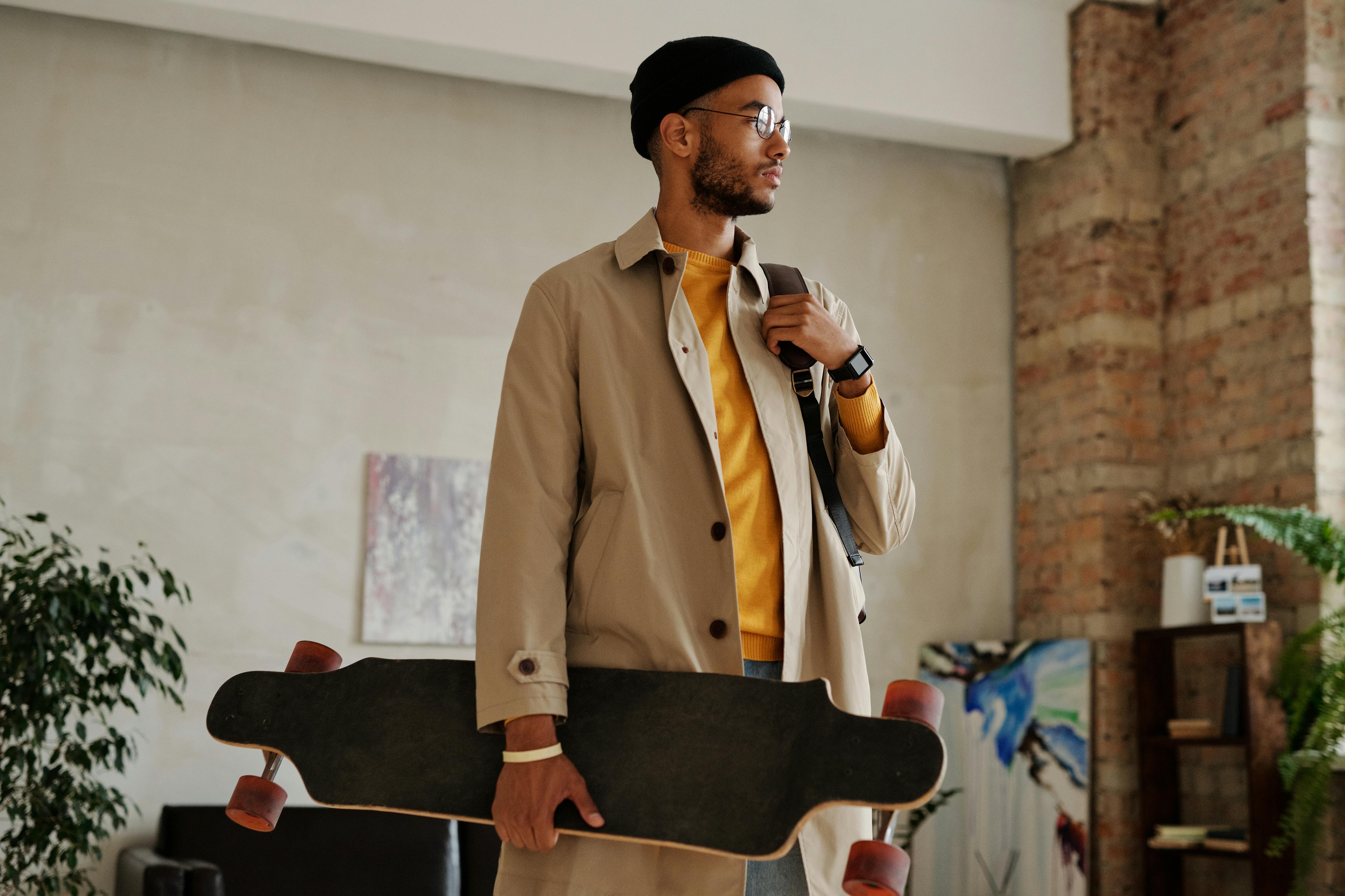 man in beige trench coat carrying a black skateboard