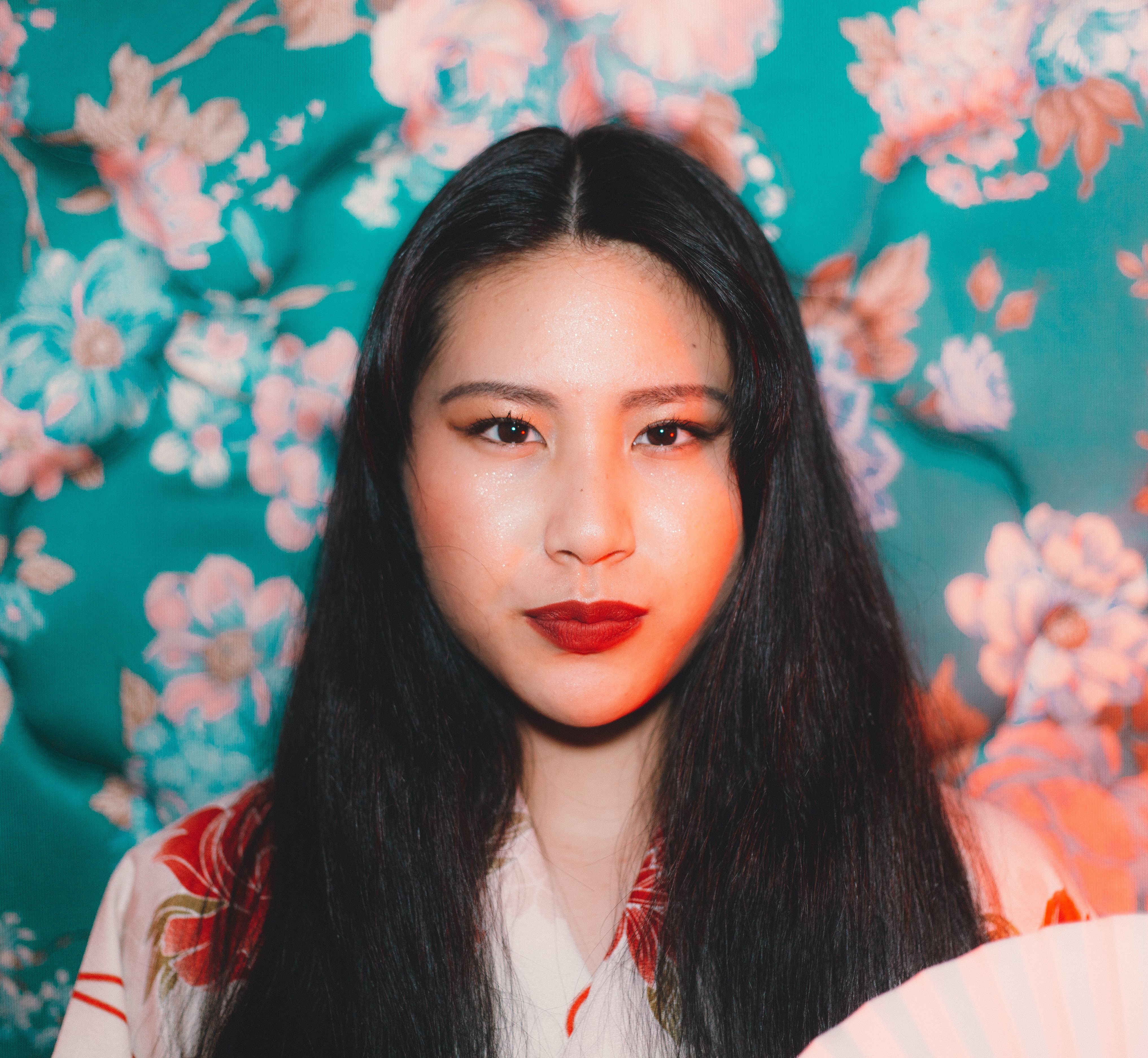 A beautiful Asian woman with long hair in traditional clothing against a floral background.