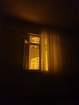 黄昏时分，舒适的内部景观中，温暖明亮的窗户和透明窗帘被打开