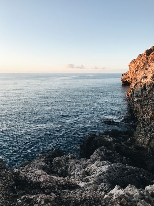 Free Tall rough rocky cliff with uneven surface located on shore near rippling endless sea against cloudless sky with horizon line in nature Stock Photo