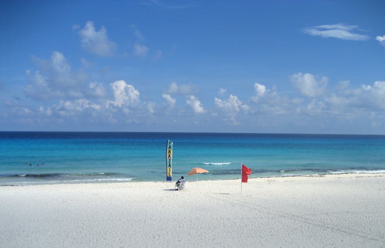 Man Sitting On An Empty Beach Next To A Parasailing Sign