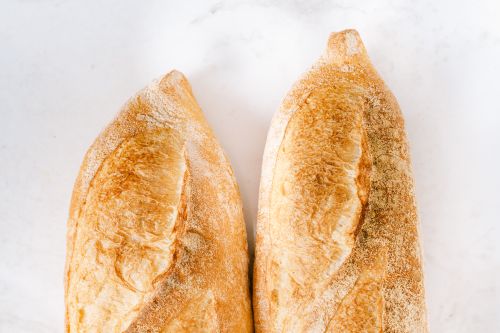 Free Two freshly baked baguettes on a white surface, showcasing golden crispy crust. Stock Photo