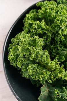 Close-up of curly kale leaves in a black ceramic bowl on marble surface. Ideal for healthy eating concepts.