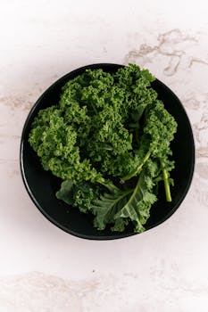 Top view of fresh kale leaves in a black bowl against a marble background. Perfect for healthy eating visuals.