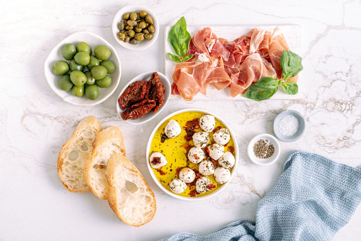 Antipasto spread of green olives, capers, sun-dried tomatoes, prosciutto, marinated mozzarella and sliced bread
