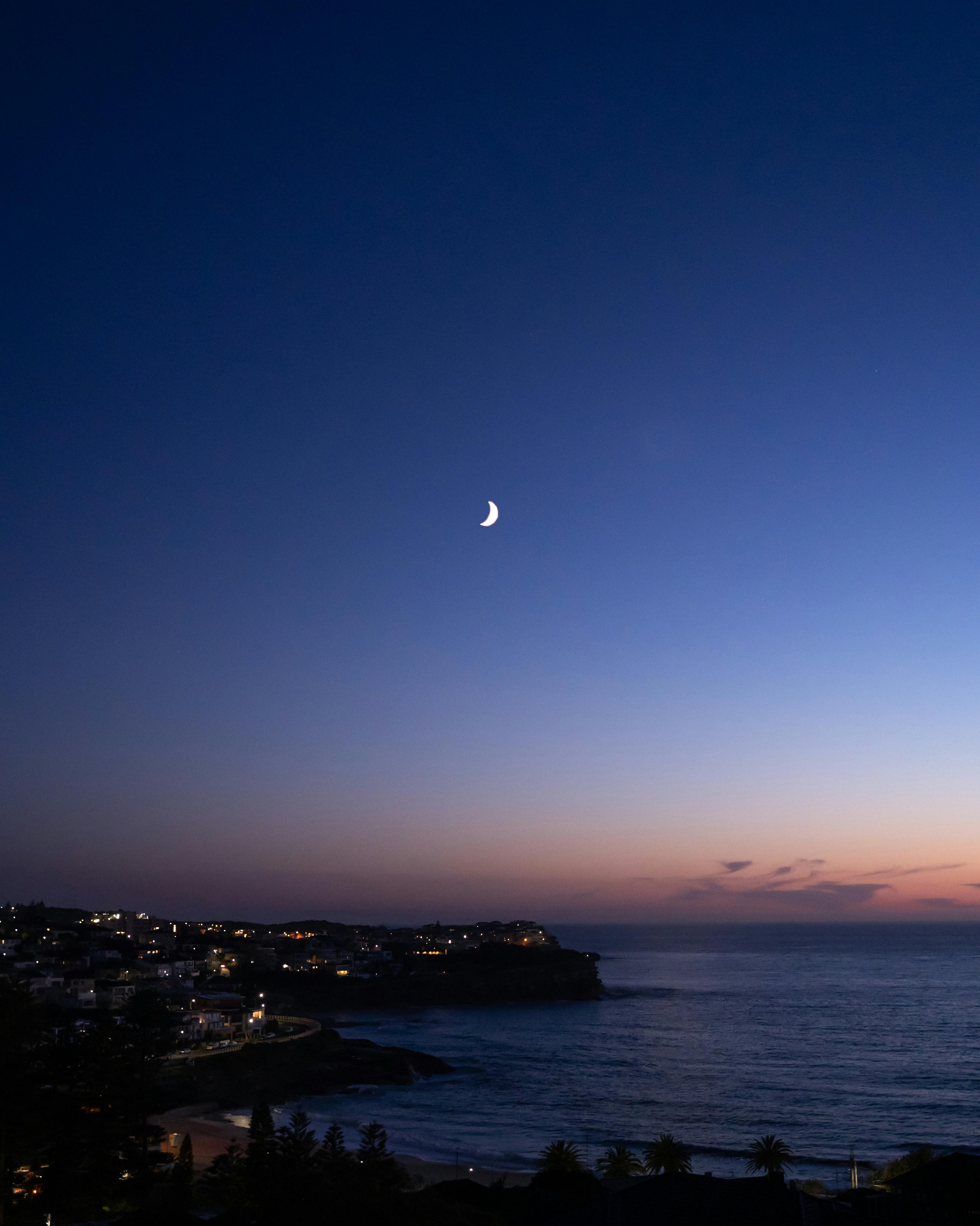 Tranquil twilight view of crescent moon over Bronte Beach's calm ocean in NSW, Australia.