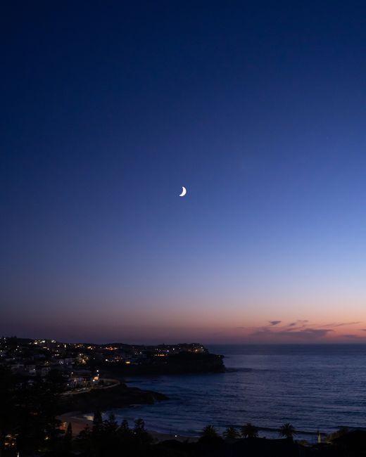 Tranquil twilight view of crescent moon over Bronte Beach's calm ocean in NSW, Australia.