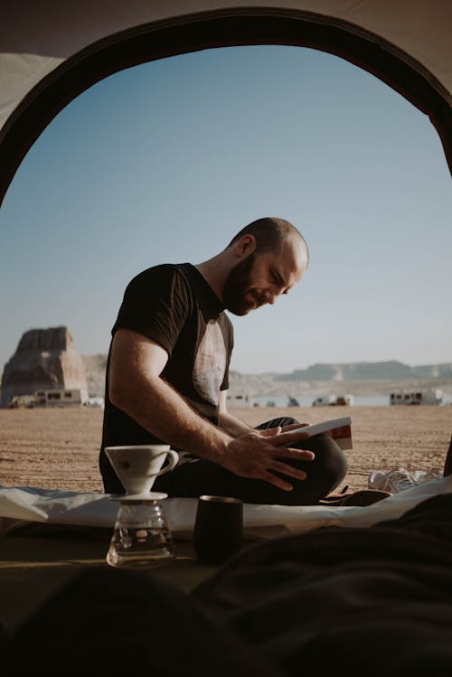 Man with coffee reading book in tent