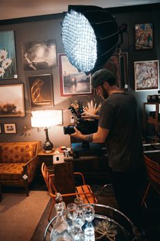 A professional cinematographer filming in a cozy, art-filled indoor setting.