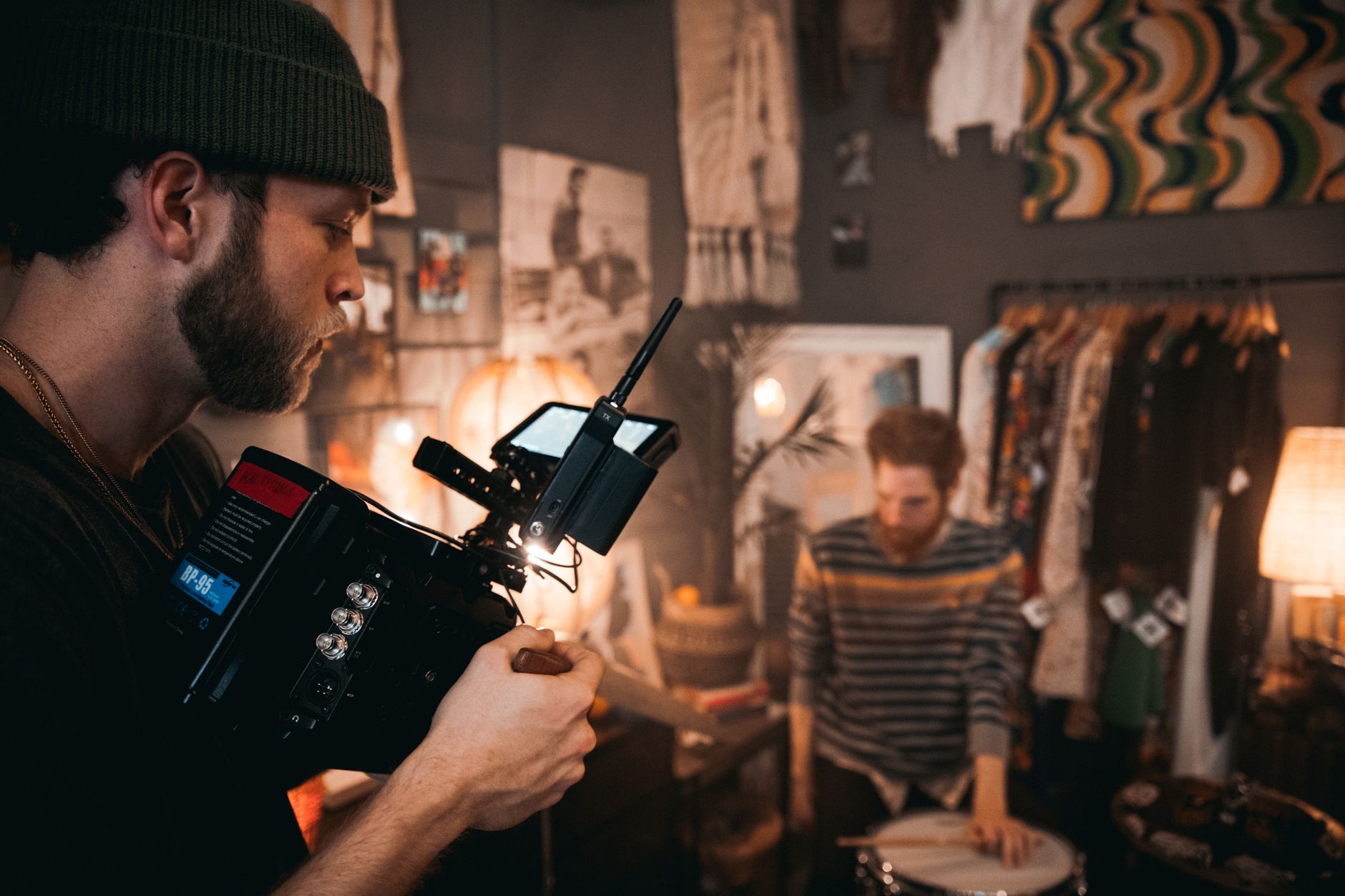 Cinematographer using camera equipment during a film shoot in a cozy studio setting with a musician.