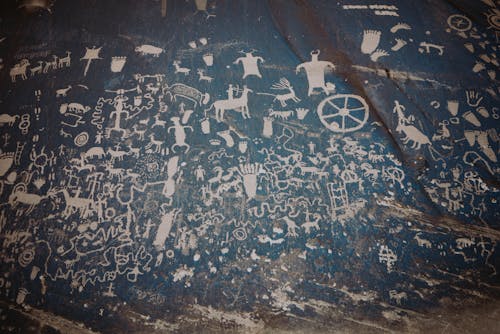 Newspaper rock with ancient symbols and petroglyphs with white paint on shabby stone blue wall with uneven surface in national park