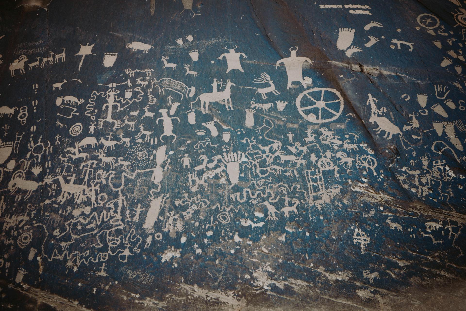 Newspaper rock with ancient symbols and petroglyphs with white paint on shabby stone blue wall with uneven surface in national park