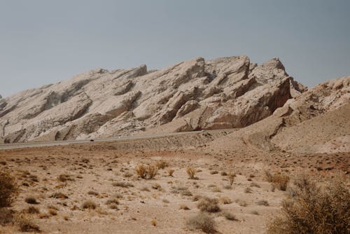 Dry desert with rare bushes and rocky cliffs with uneven surface located in mountainous area against cloudless sky in nature