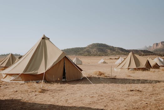 A tranquil campsite featuring multiple canvas tents in an arid desert landscape under a clear sky.