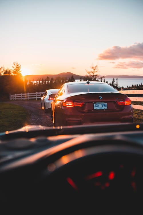 Through windshield glass of modern cars riding along rural road near calm lake surrounded by trees against sunset sky