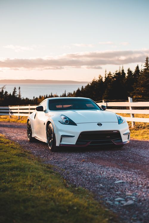 Free Trendy sports car parked on rough road near fenced meadow and lush trees growing at lakeside against sunset sky Stock Photo