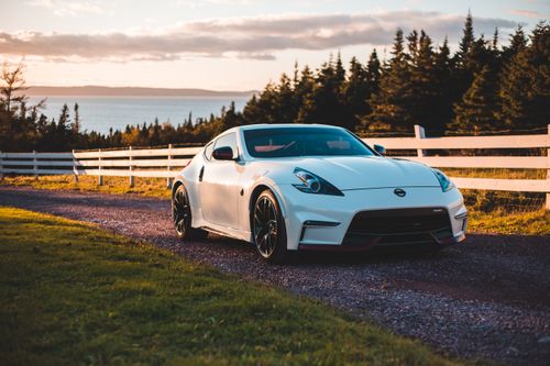 Free Stylish white coupe car parked near paddock surrounded by spruce trees growing on lake shore at sunset Stock Photo