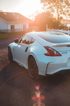 From above of trendy white coupe car parked near cozy small house in countryside at sunset