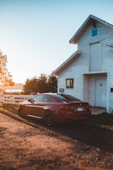Contemporary car parked near white wooden cottage in countryside under cloudless blue sky in sunny day
