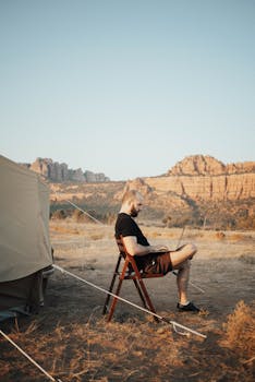 Man working on a laptop at a desert campsite, showcasing remote work lifestyle.