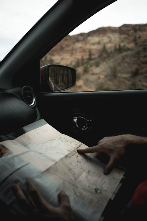 Crop faceless male traveler sitting in car and looking route in map during journey