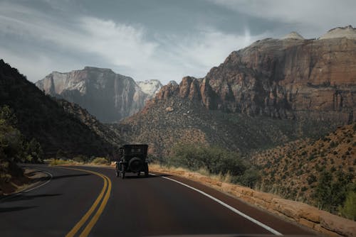 Vintage automobile on asphalt road between rough rock formations with vegetation under cloudy sky